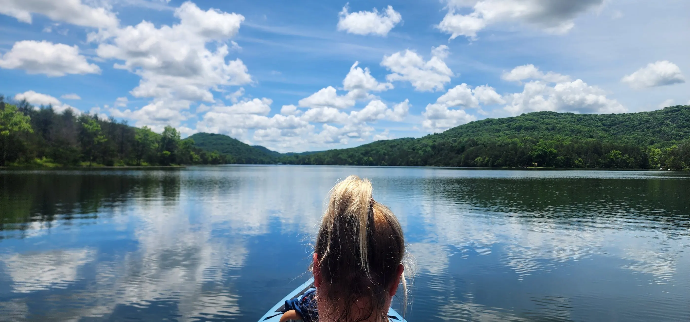Brittnay kayaking on a calm lake under a big blue sky with puffy clouds
